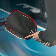 Person holding a pickleball paddle with a blurred sports court background