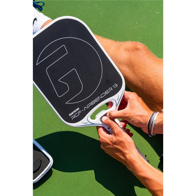 Person holding a pickleball paddle with a close-up of the brand logo on a green court background