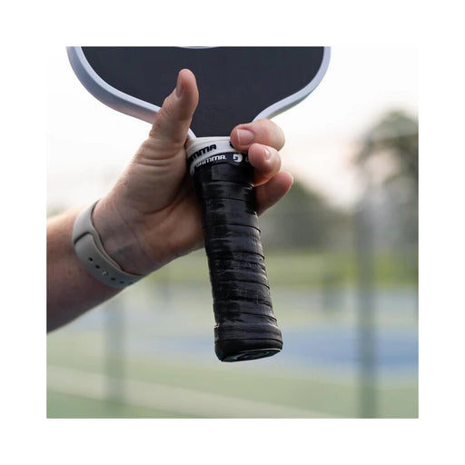 Hand holding a pickleball paddle with a blurred outdoor background