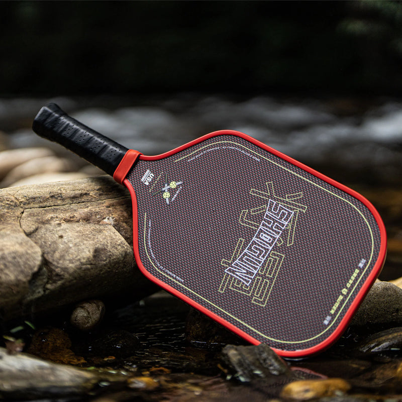Pickleball paddle with red border on a natural background