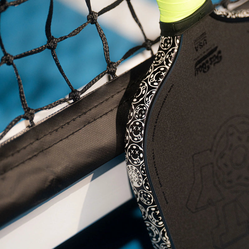 Close-up of a pickleball paddle hitting a pickleball against a blue background