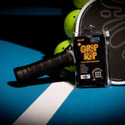 Grip and Rip tennis racket grip enhancer packaging on a tennis racket with balls in the background.