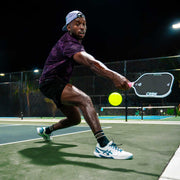Person playing pickleball on an outdoor court at night