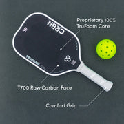 Pickleball paddle with T700 raw carbon face and TruFoam core, next to a green pickleball on a dark background.