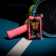 Pink tennis racket grip with 'Grip It' packaging on a blue surface