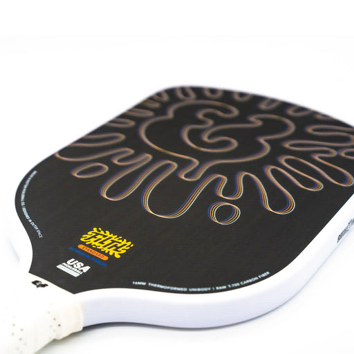 Close-up of a pickleball paddle with a black design and white handle on a white background