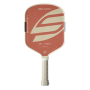 A Selkirk Labs pickleball paddle featuring a terracotta orange face with a large cream-colored abstract logo, a cream-colored edge trim, and a textured cream grip handle.