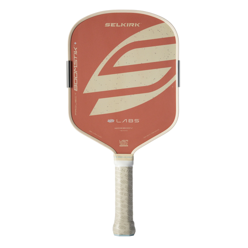 A Selkirk Labs pickleball paddle featuring a terracotta orange face with a large cream-colored abstract logo, a cream-colored edge trim, and a textured cream grip handle.