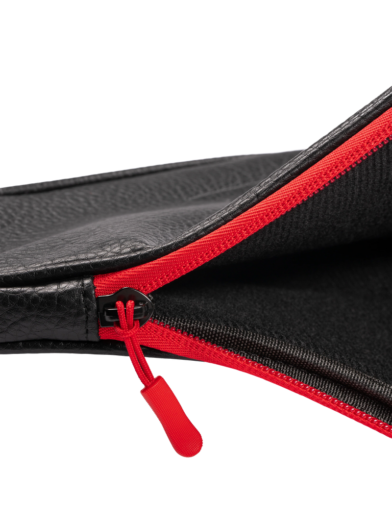 Close-up of a black leather bag with a red zipper on a white background