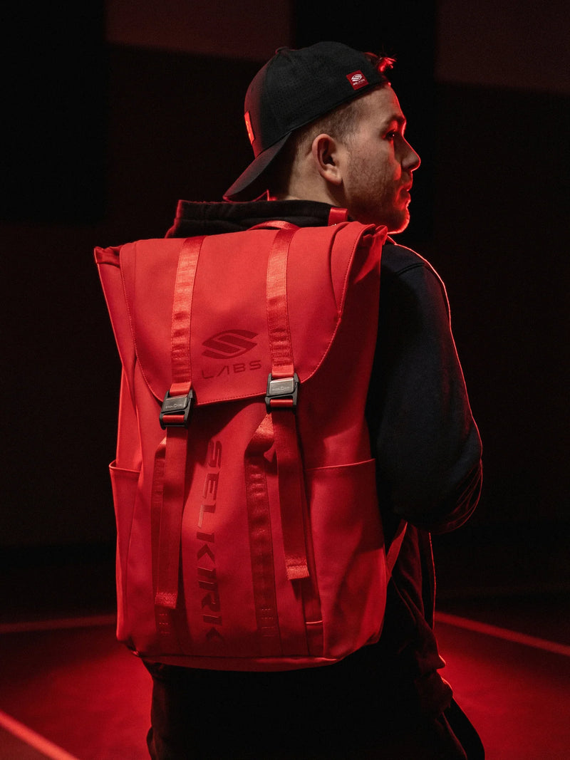 Person wearing a red backpack with a brand logo on a dark background